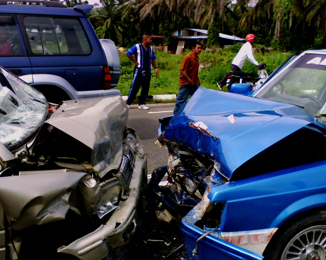 Dois carros com a frente completamente destruída, encostados um no outro numa estrada após batida de frente.
