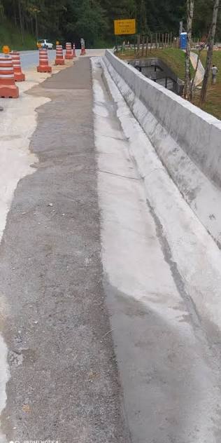 Barreira New Jersey de concreto recém-construída correndo à margem de uma rodovia, com cones e barreiras portáteis sinalizando a obra.