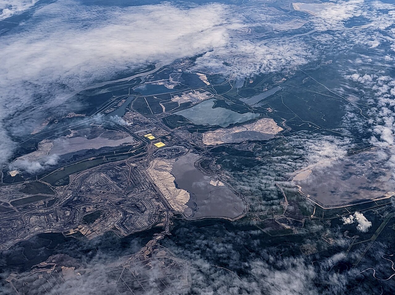 Mina de areias betuminosas em Alberta, no Canadá, com máquinas escavando o solo escuro encharcado de betume.